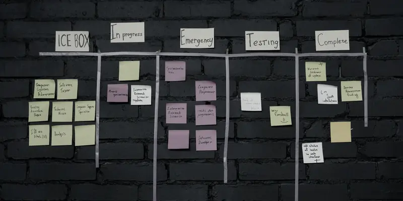 A wall-mounted kanban board on dark brick, sticky notes grouped under handwritten column headings.